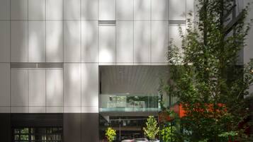 A modern building with a glass facade, outdoor seating area, and a tree.