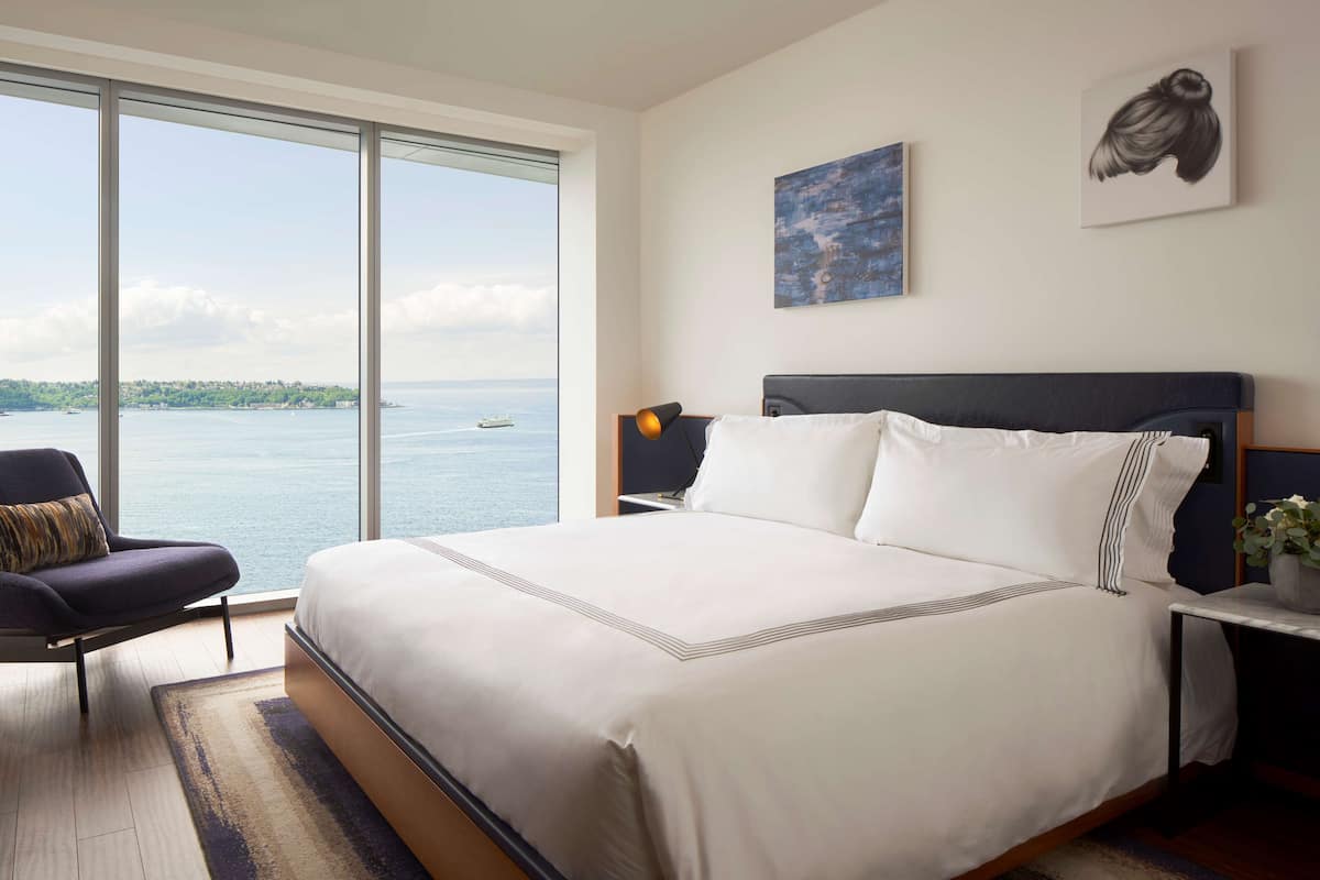 Quarto com cama grande, uma cadeira, mesa de cabeceira e vista para o mar.