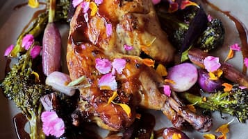 Un plato de pato asado con verduras y flores comestibles.