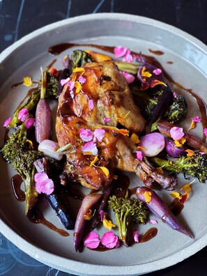 A plate of roasted duck with vegetables and edible flowers.