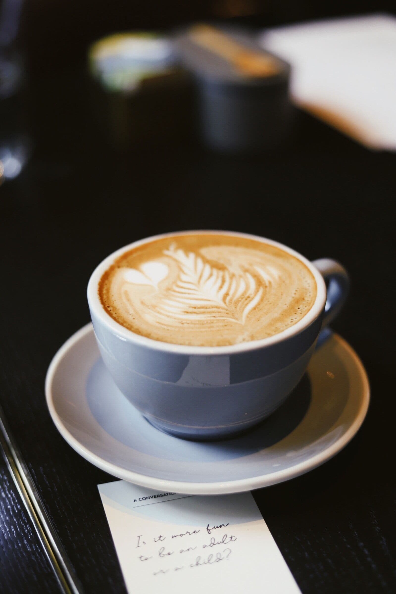 Una taza de café con arte de latte sobre un plato, colocada sobre una mesa con un menú.