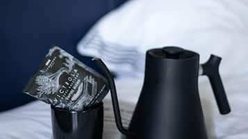 A bed with a black kettle and a mug on a newspaper.