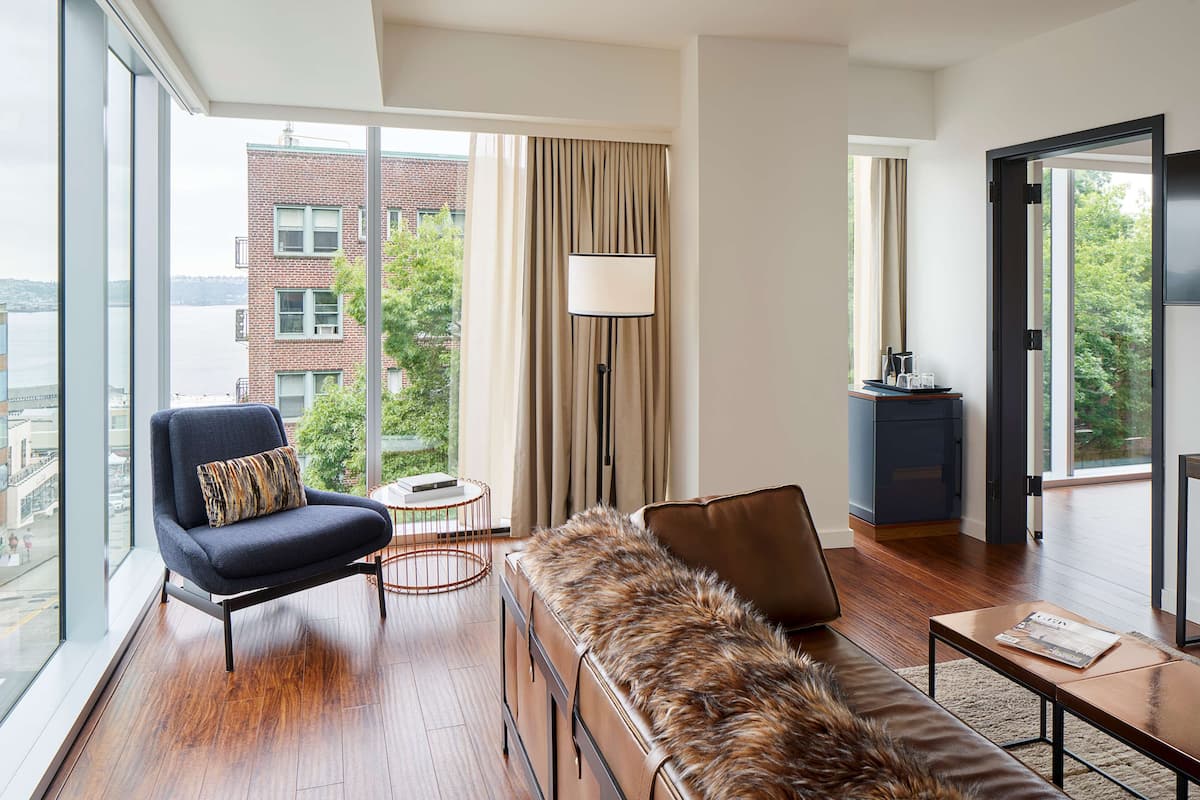 Sala de estar moderna com uma janela ampla, um sofá, uma poltrona, um abajur e vista para um edifício.