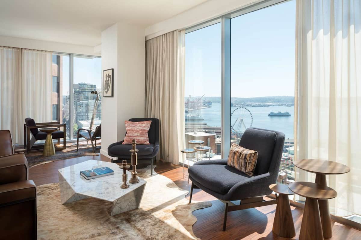 Uma sala de estar moderna com uma grande janela que oferece vista para a cidade, um sofá confortável, uma mesa de centro e uma pequena mesa lateral.