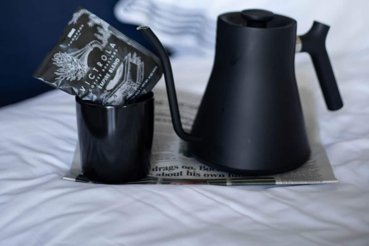 Uma cama com uma chaleira preta e um pacote de café sobre um jornal.