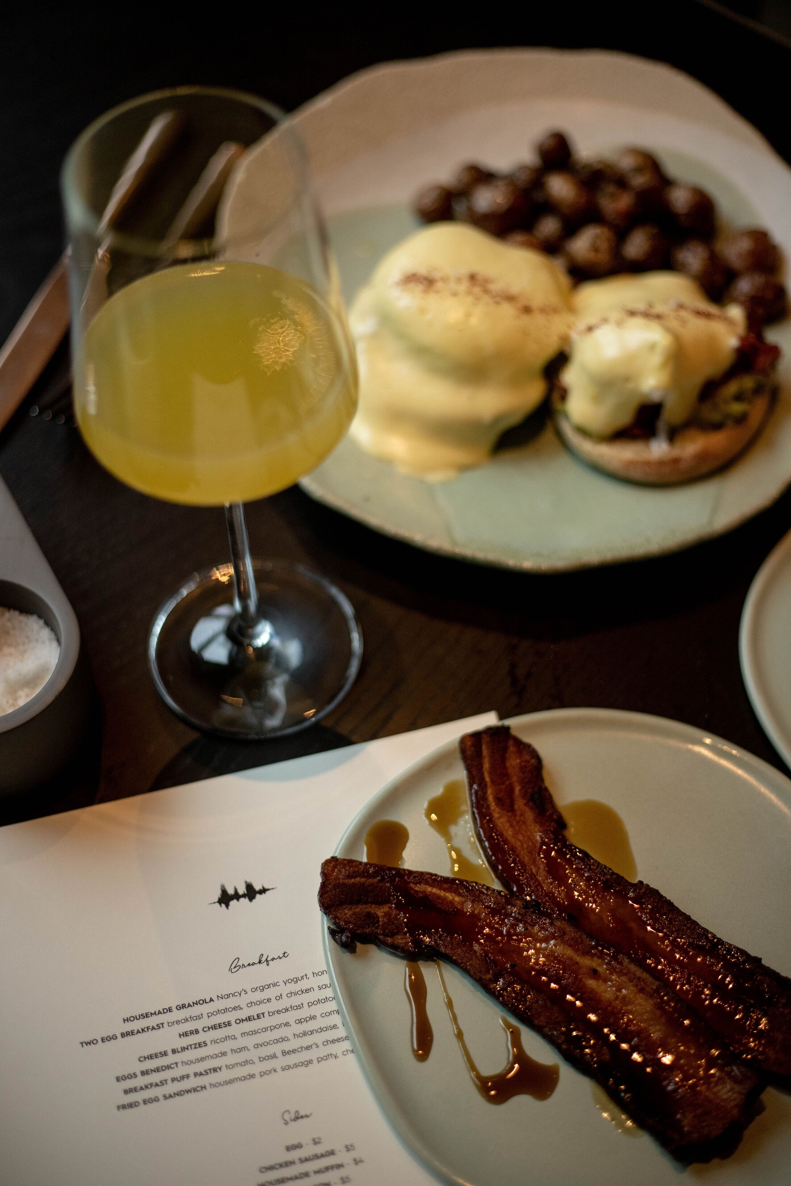 Un plato de desayuno con tocino, huevos Benedict y un vaso de jugo de naranja.