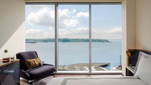 A bedroom with a large window offering a view of the sea and a distant island. - Thompson Seattle, by Hyatt (Seattle)