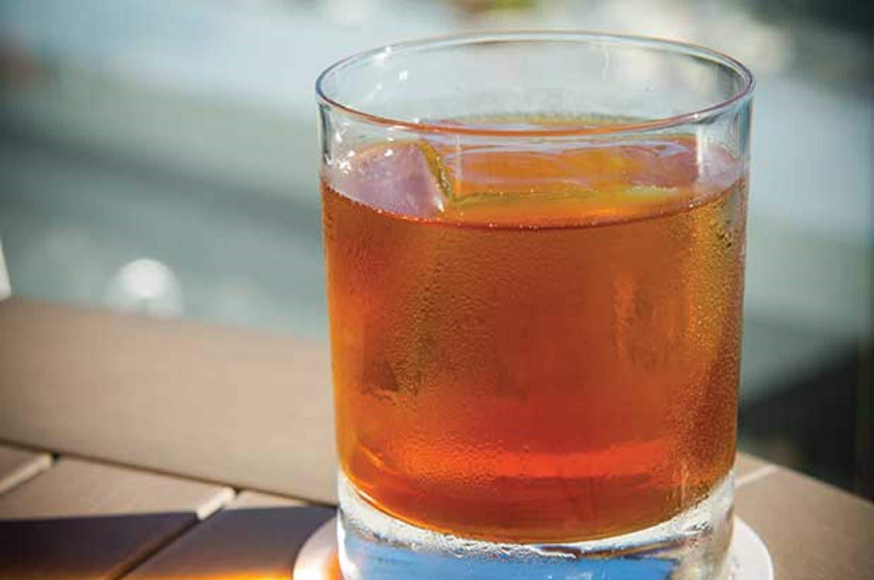 Een glas amberkleurig drankje met ijsblokjes, geplaatst op een tafel met een onscherpe achtergrond.