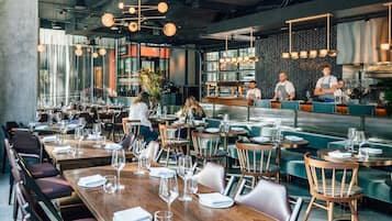 Ein modernes Restaurant mit Holztischen und -stühlen, einer Bar und einer Küche im Hintergrund.