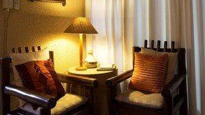 A cozy seating area with two wooden chairs, a small table with a lamp, and a wall-mounted picture frame. - A Traveller's Palm (Phalaborwa)