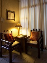 A cozy seating area with two wooden chairs, a small table with a lamp, and a wall-mounted picture frame.