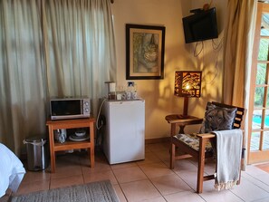 A compact living space with a microwave, refrigerator, and a small table with a lamp. - A Traveller's Palm (Phalaborwa)