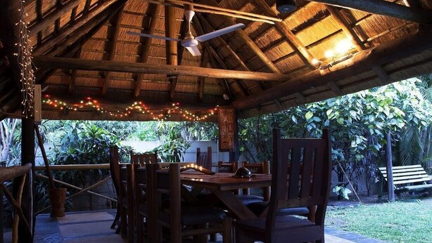 An outdoor dining area with wooden furniture and a thatched roof. - A Traveller's Palm (Phalaborwa)