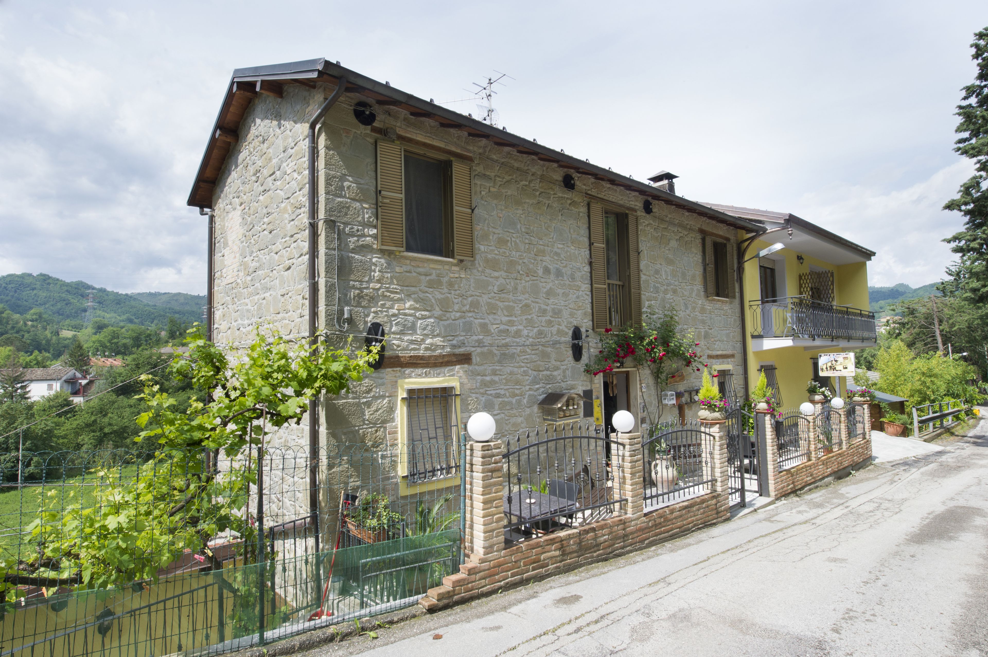 Une maison en pierre avec un balcon, un jardin clôturé et un paysage montagneux en arrière-plan.