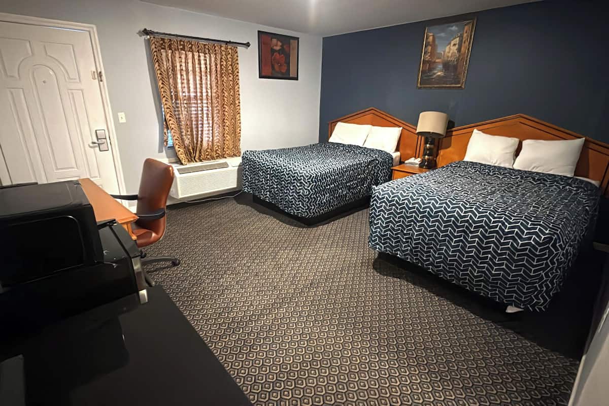 Habitación de hotel con dos camas, un escritorio, una silla, una ventana con cortinas y un cuadro en la pared.