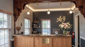 A reception desk with a 'NO PETS' sign, wooden paneling, a wall-mounted light fixture, and a flower arrangement. - At 9 Motel Near Freehold I-195 (Howell)