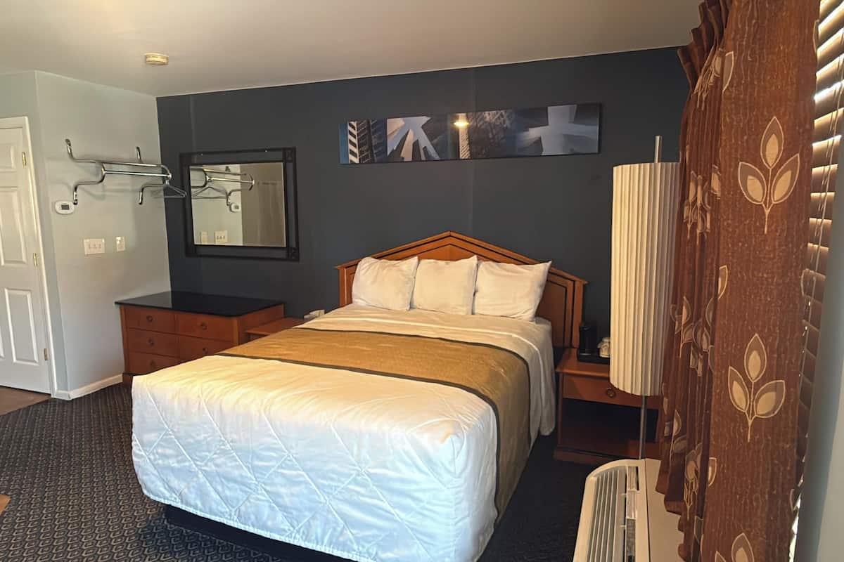 Habitación de hotel con una cama, tocador, espejo y ventana con persianas.