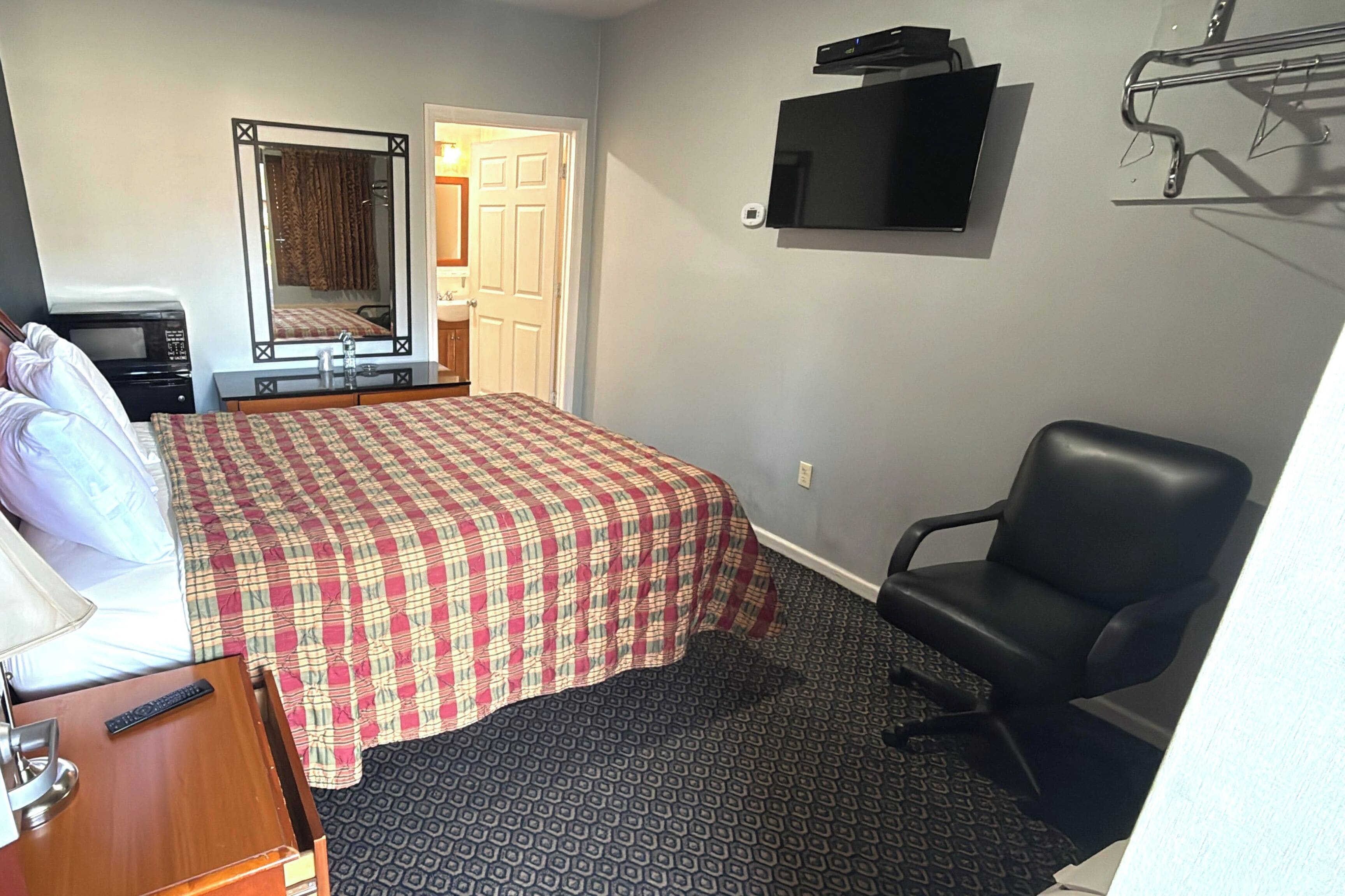 A hotel room with a bed, a desk, a chair, a television, and a door leading to a bathroom.