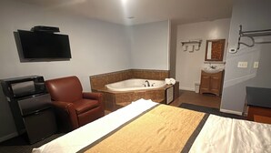 A hotel room with a bed, a TV, a brown leather chair, a bathtub, a sink, and a mirror. - At 9 Motel Near Freehold I-195 (Howell)