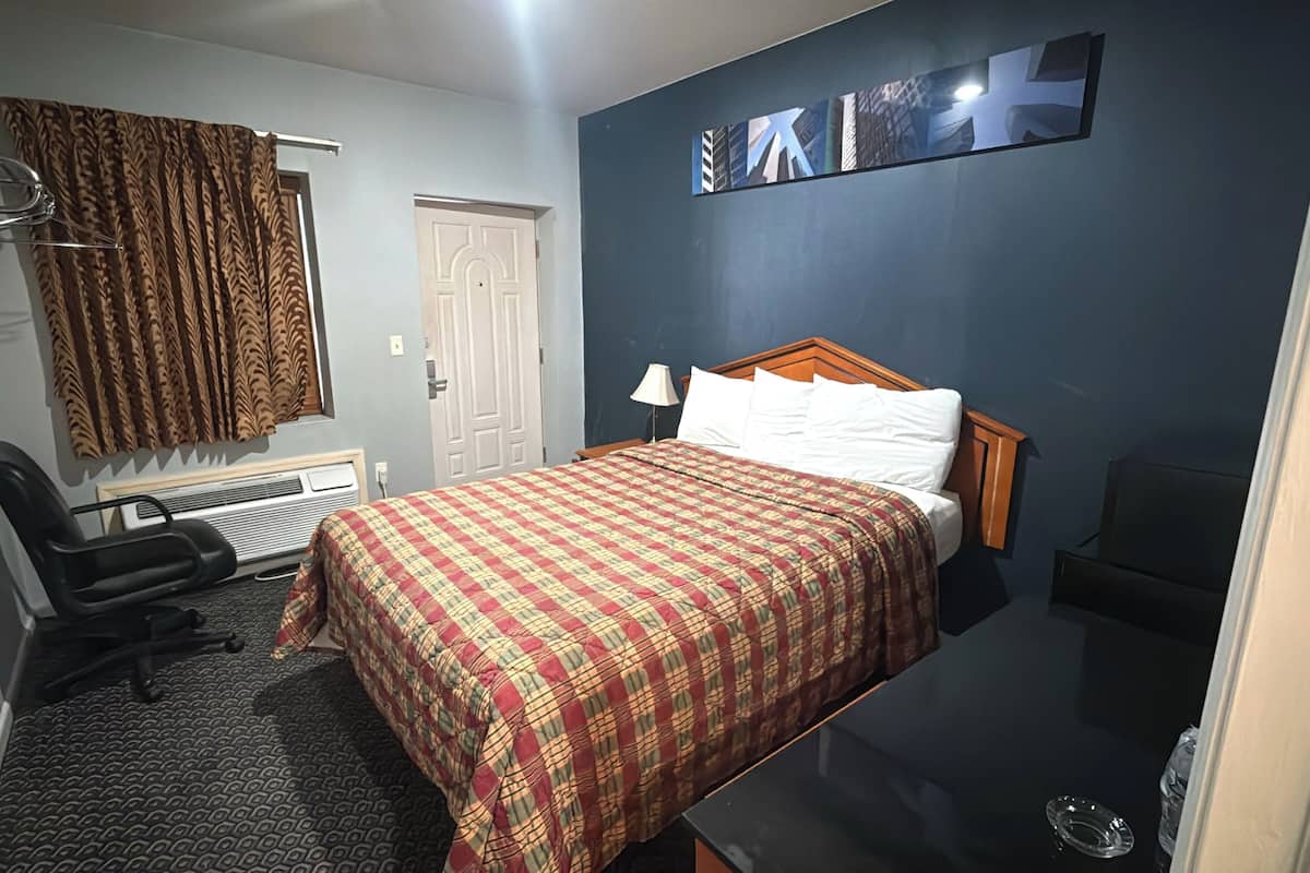 Una habitación de hotel con cama, una silla, un escritorio, un calentador y una pared decorada con obras de arte.