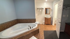 A bathroom with a large bathtub, a sink, a mirror, and a door leading to another room. - At 9 Motel Near Freehold I-195 (Howell)