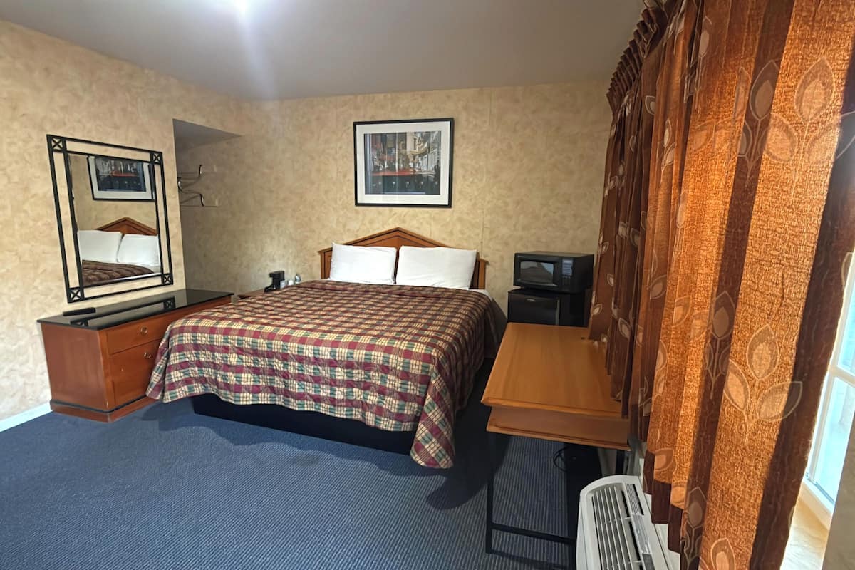 Habitación de hotel con cama, escritorio, silla, televisión, espejo y ventana con cortinas.