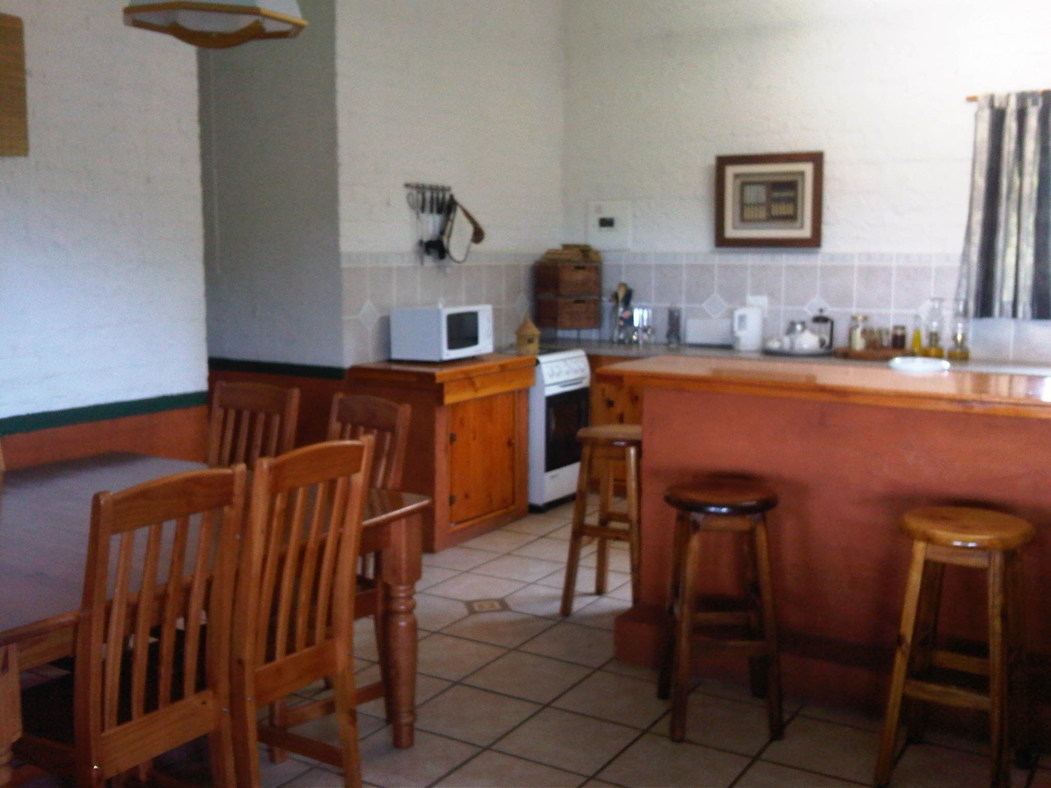 A kitchen with wooden chairs, a bar stool, a microwave, and a stove.