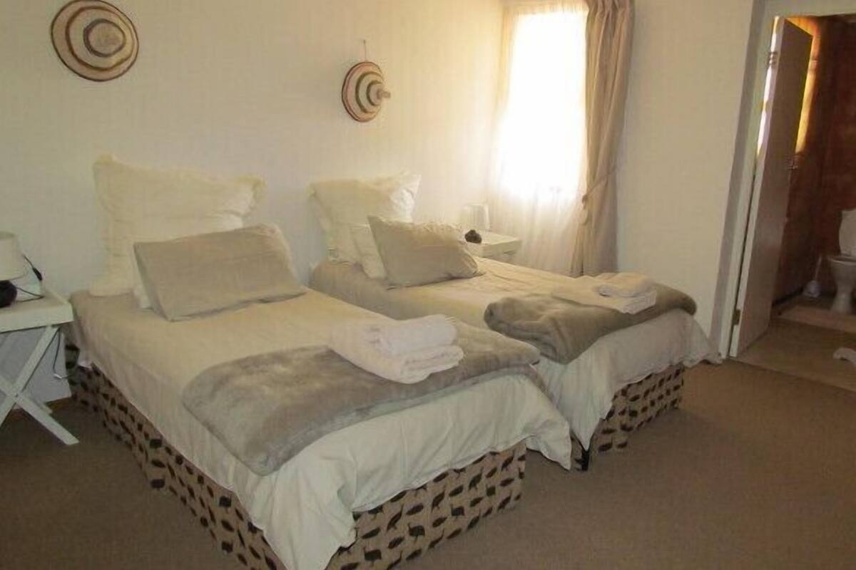 A double bed with two pillows and a blanket, a bedside table with a lamp, and a window with curtains.