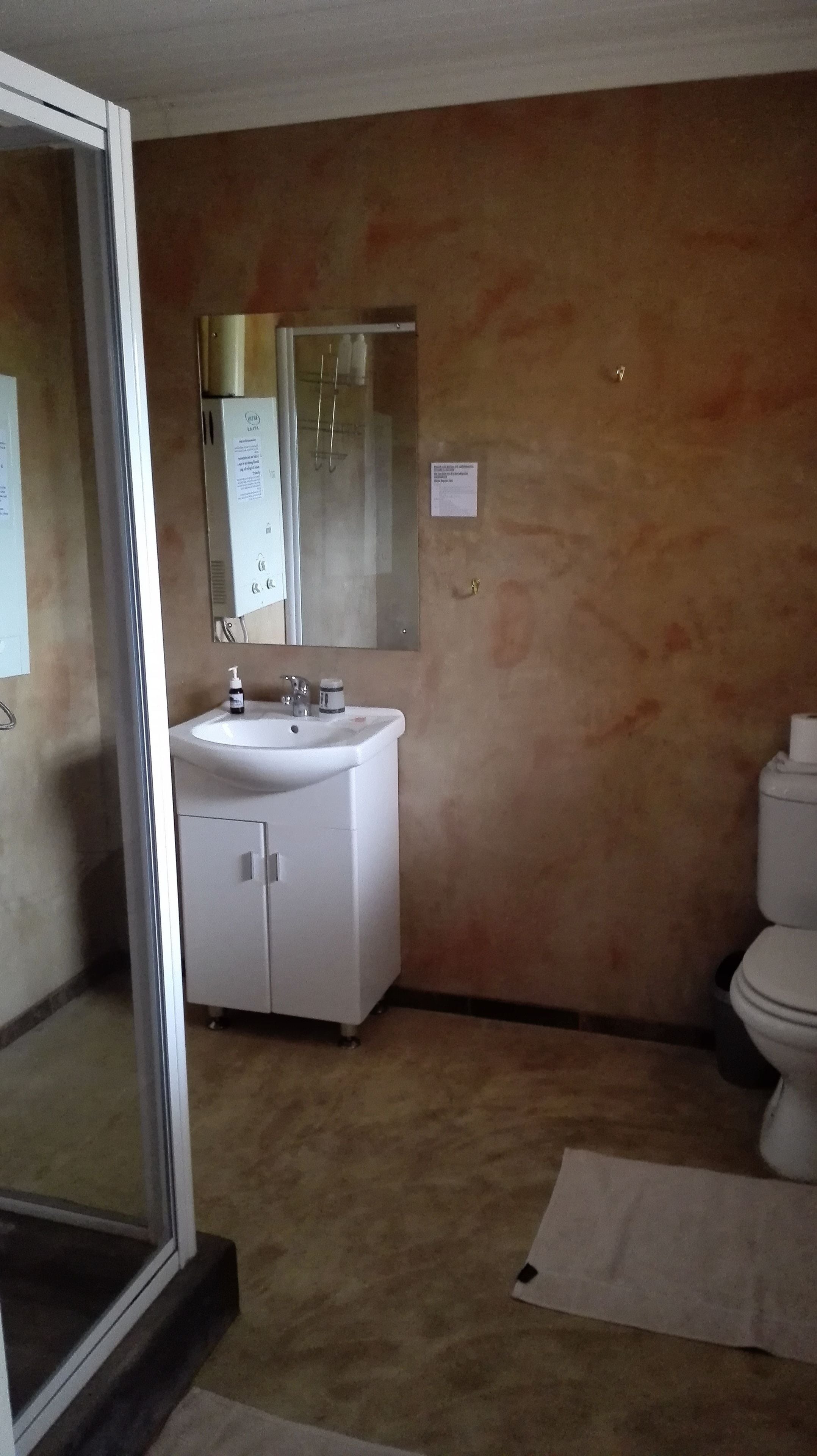 A bathroom with a white sink, mirror, and toilet. There is a beige wall and a glass shower door.