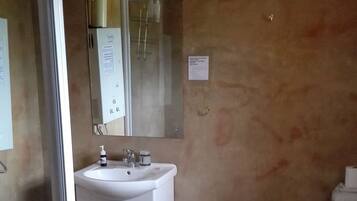 A bathroom with a white sink, mirror, and toilet. There is a beige wall and a glass shower door.