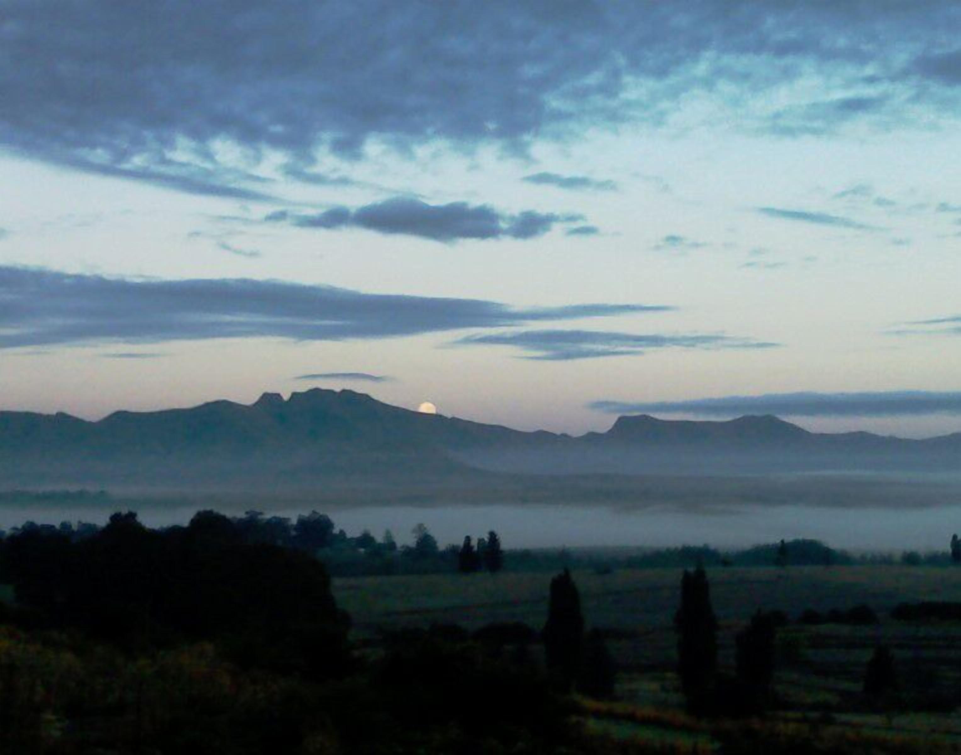 Paesaggio con montagne sullo sfondo, cielo sereno e una piccola fonte di luce all'orizzonte.