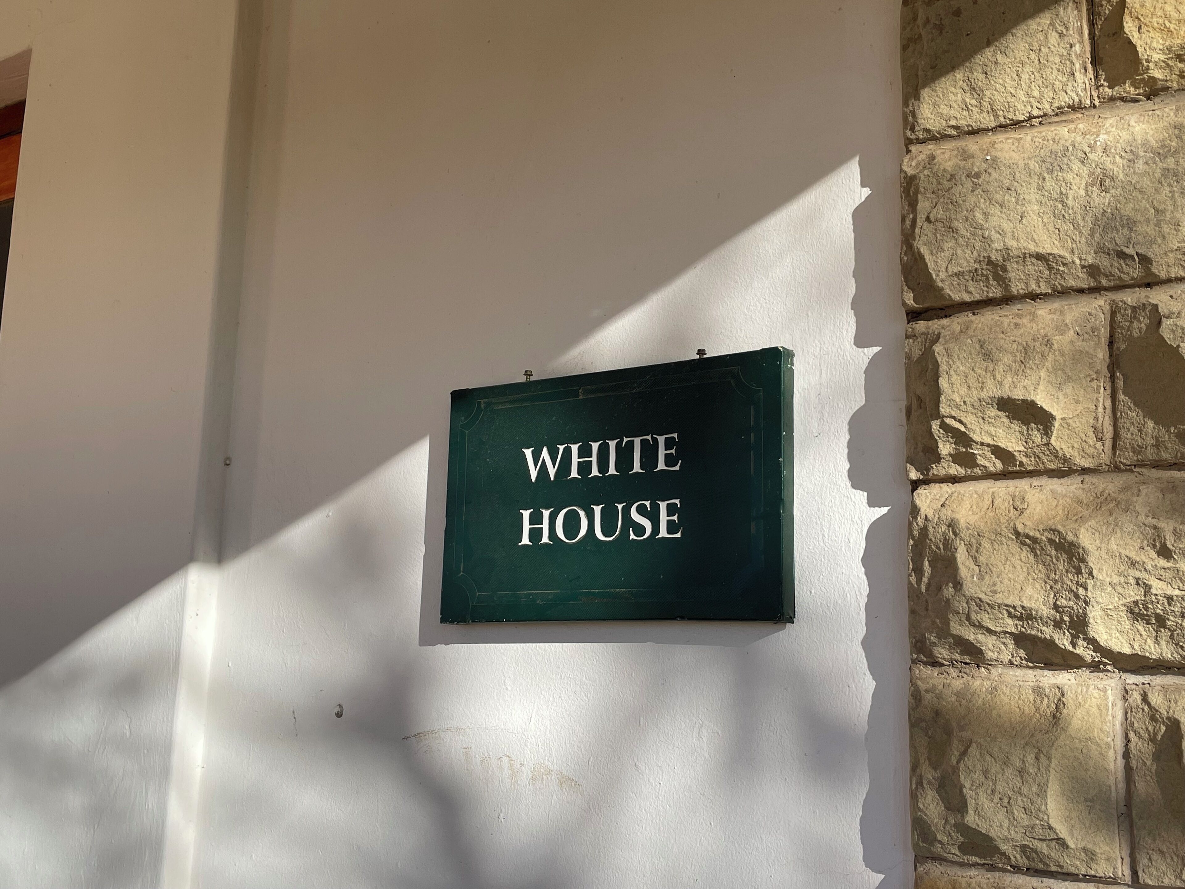 A sign that reads "WHITE HOUSE" mounted on a wall with a stone wall to the right.