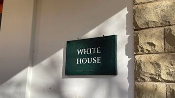 A sign that reads "WHITE HOUSE" mounted on a wall with a stone wall to the right.