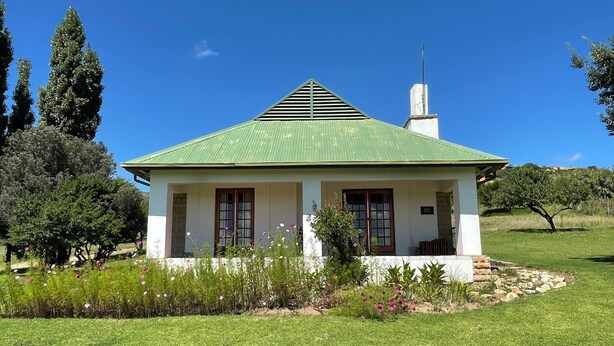 A small, single-story building with a green roof, surrounded by a well-maintained lawn and various plants. - Pumula Guest Farm (Fouriesburg)