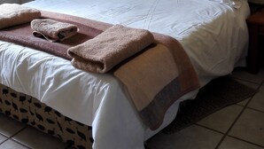A neatly made bed with white bedding and a brown throw blanket, a bedside lamp, and a wall with three woven hats. - Pumula Guest Farm (Fouriesburg)