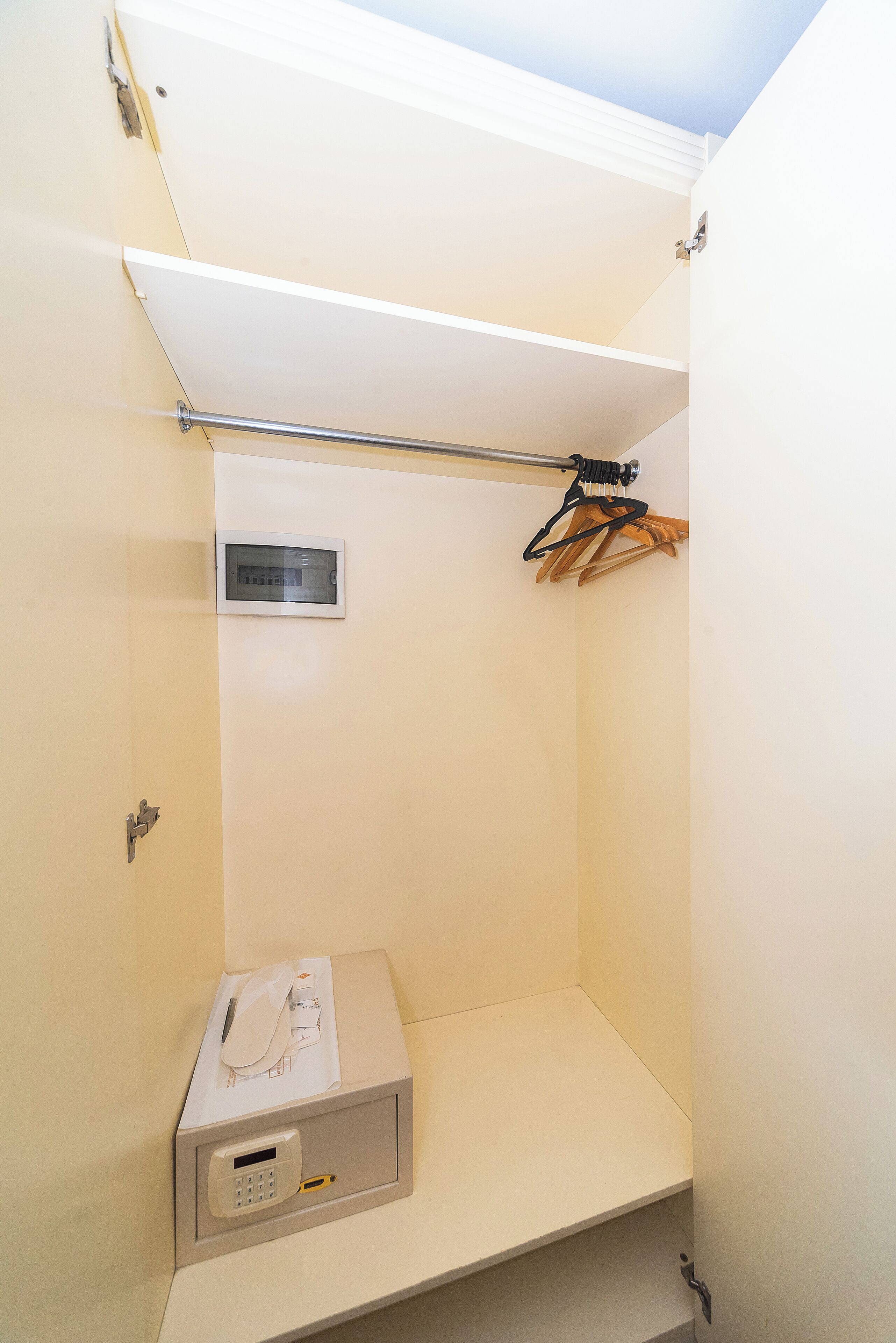 Un cuarto pequeño y cerrado con paredes blancas, una estantería metálica, un panel de control y una percha.
