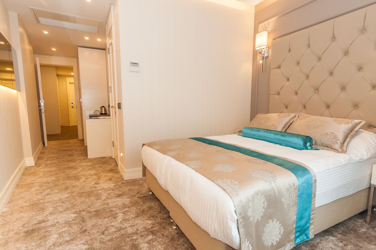 A bedroom with a large bed, a headboard, a nightstand, and a wall-mounted lamp.