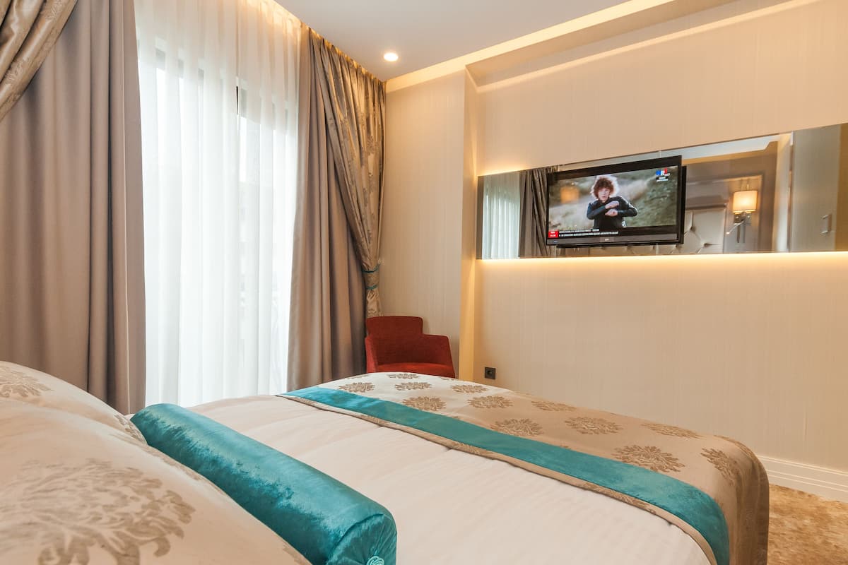 A hotel room with a bed, a television mounted on the wall, and a red chair.