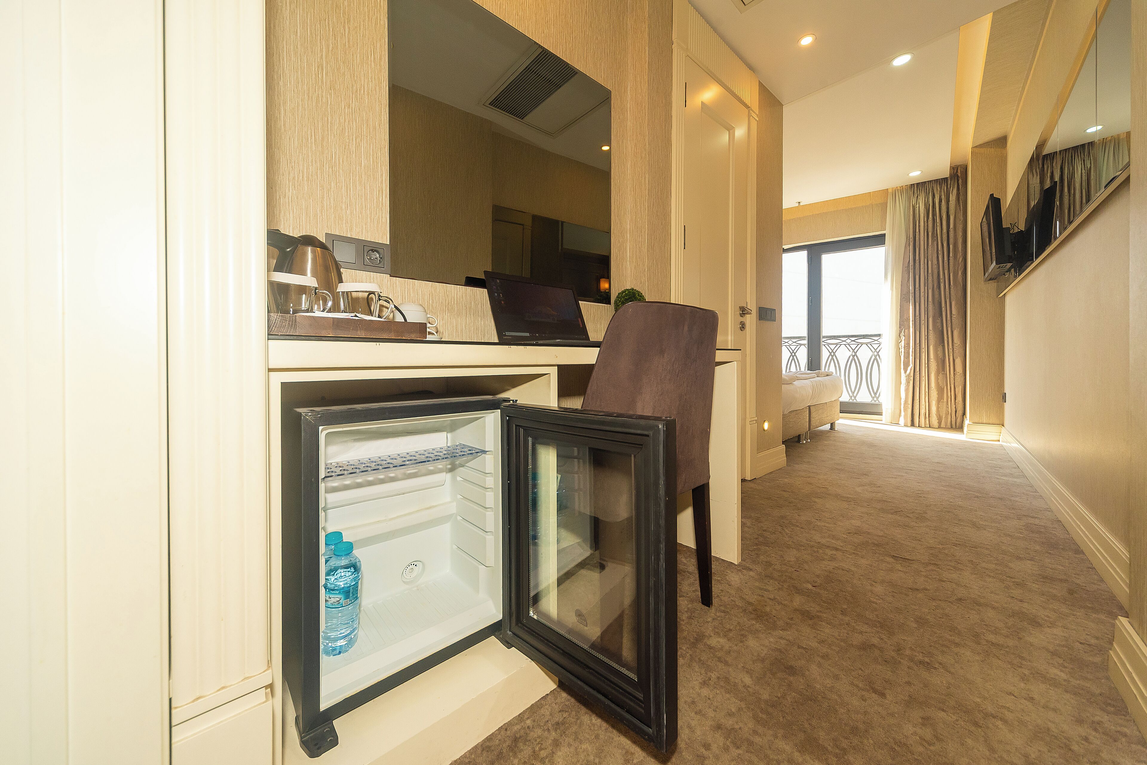 A hotel room with a kitchenette, a refrigerator, a laptop, a chair, and a bed.