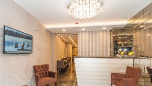 En modern hotellobby med en receptionsdisk, bekväma sittplatser, en kristallkrona och en stor tv-skärm som visar ett snötäckt landskap.