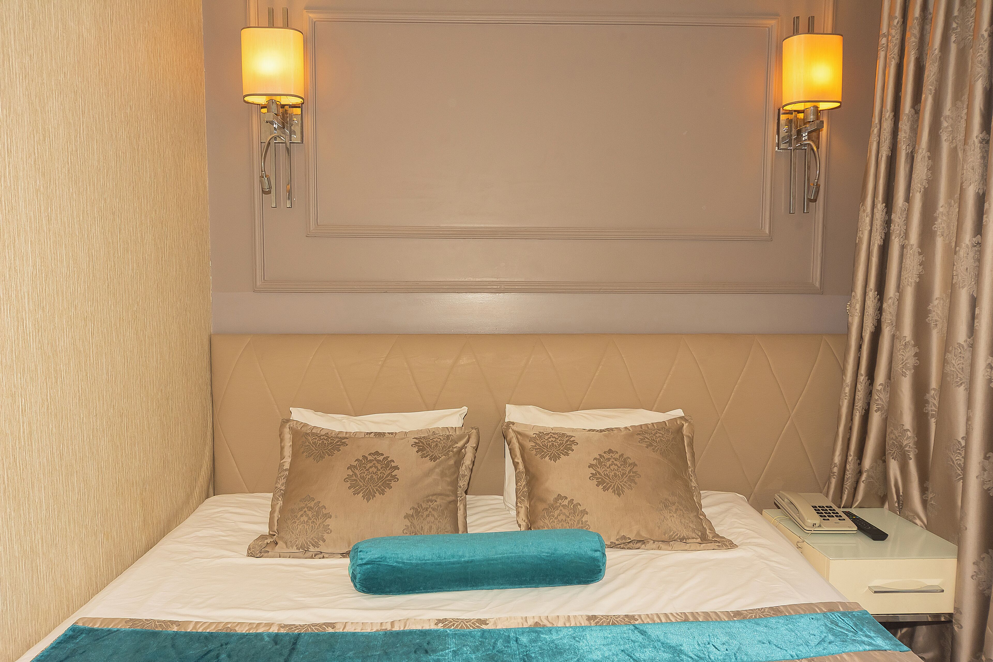 Hotelkamer met een bed, twee wandlampen, een nachtkastje met telefoon en een gordijn.