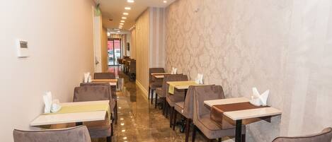 Un restaurante con una distribución alargada y estrecha, varias mesas y sillas, y un piso pulido.