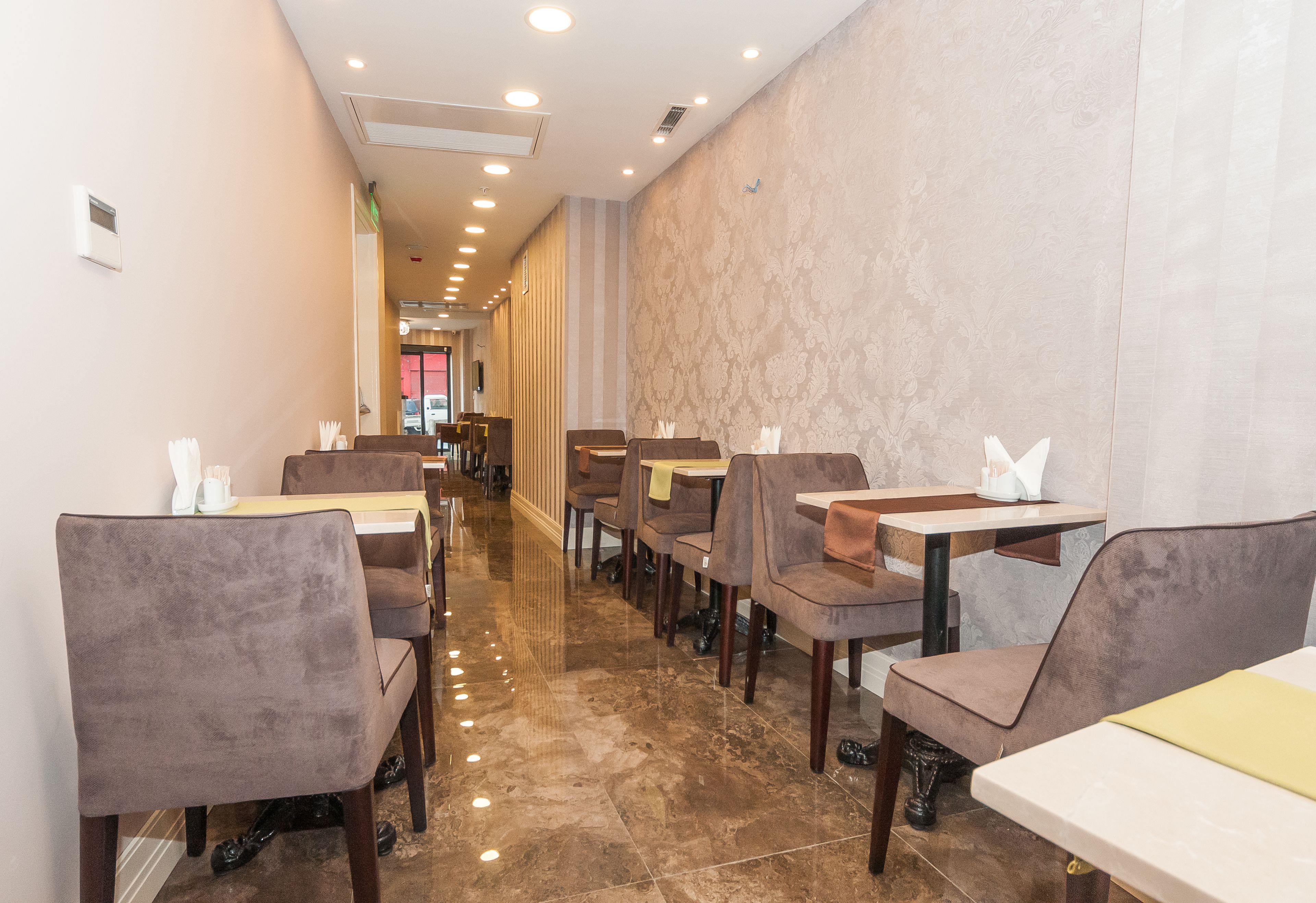 A restaurant with a long, narrow layout, featuring rows of tables and chairs along a central aisle.