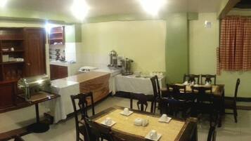 A dining area with multiple tables and chairs, a kitchen area with a coffee machine, and a television mounted on the wall.