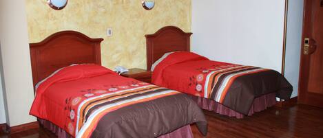 Dos camas individuales con cabeceros de madera, colchas rojas y marrones, y suelo de madera.