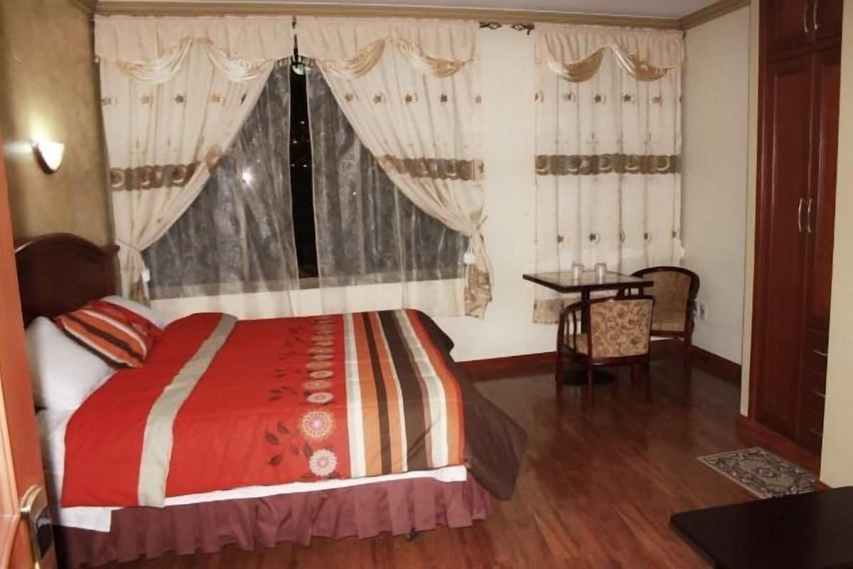 A bedroom with a bed, a small table with chairs, and a wardrobe.