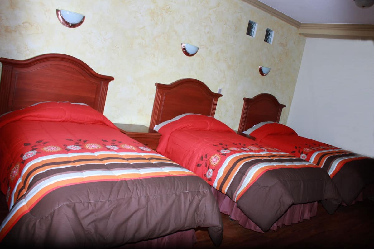 A room with two wooden beds, each with a red and brown bedspread.