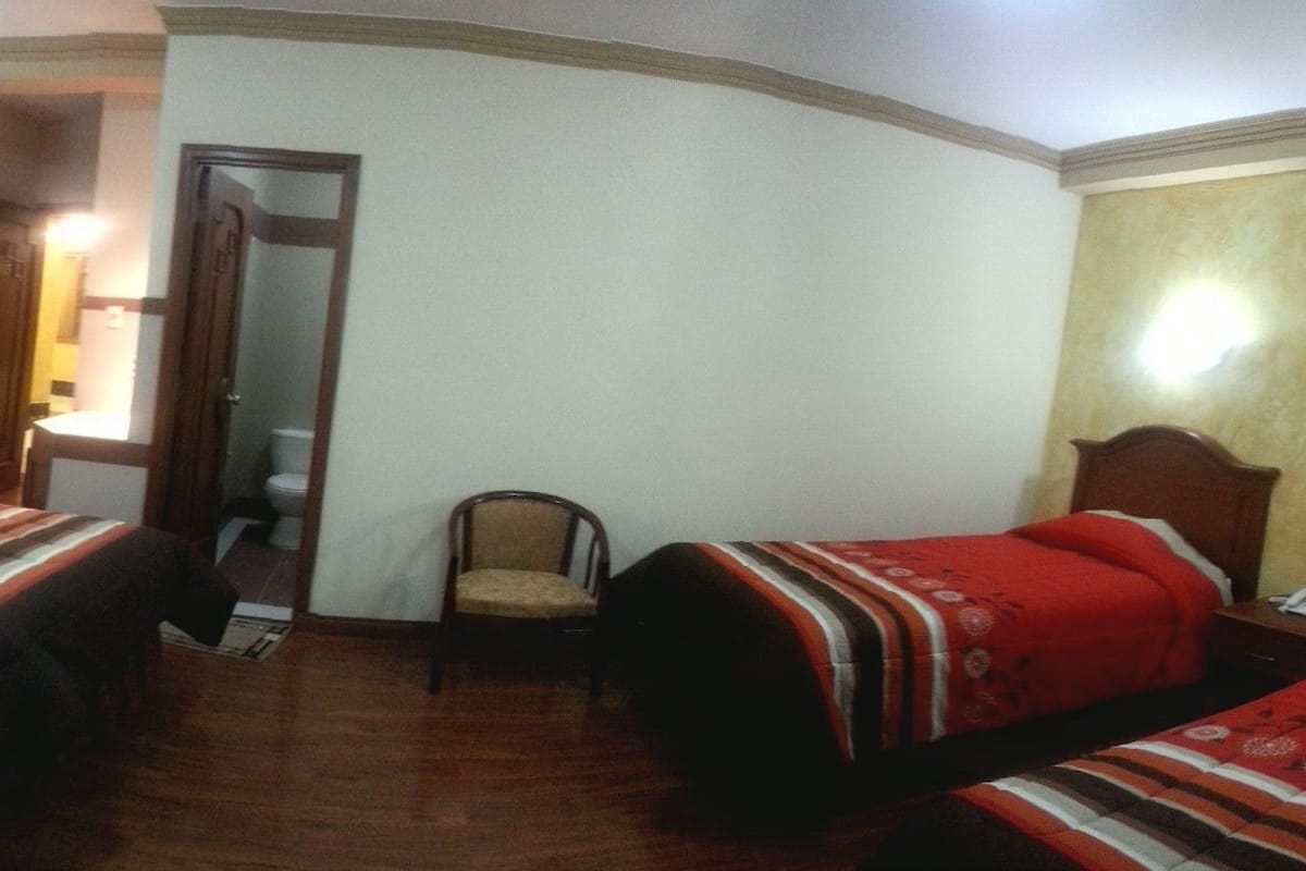 A room with three single beds, a wooden floor, and a mirror on the wall.