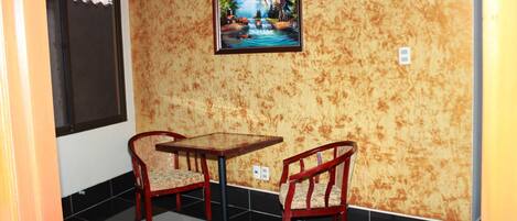 Una habitación pequeña con pared de madera, un televisor sobre una mesa y dos sillas, y una ventana a la izquierda.