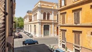 A street view with parked cars and scooters, buildings with classic architecture, and a clear sky. - Da Me Suites (Rome)